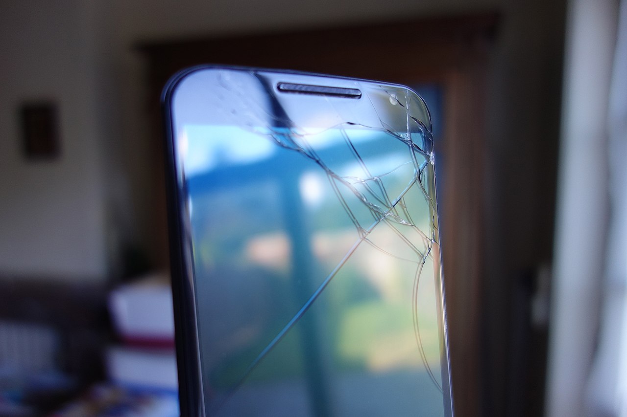 Cracked smartphone screen, with garden reflected on it.